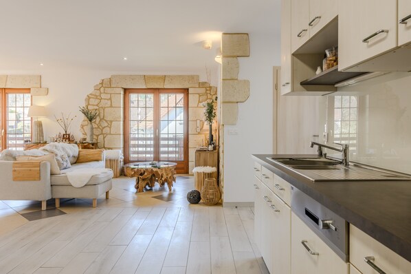 Una cocina moderna con armarios blancos, un lavamanos de acero inoxidable y una pared de piedra.