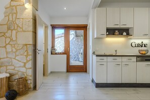 A modern kitchen with white cabinets, a stone wall, and a wooden door leading to a balcony.