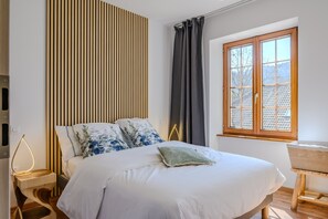 Una camera da letto con un letto, un comodino con una lampada, una finestra con tende e vista sull'esterno.