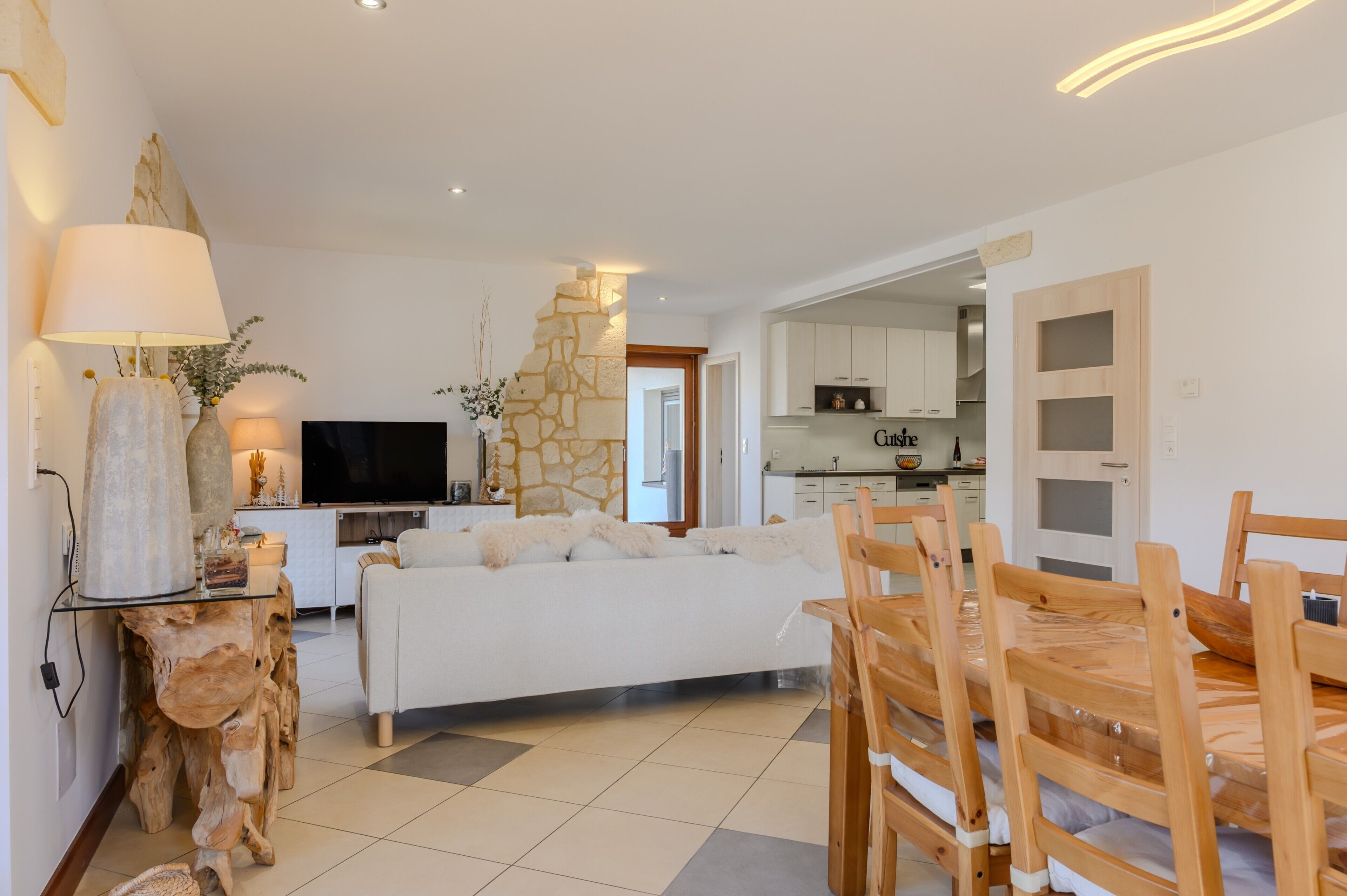 Un salon moderne avec un canapé, une table à manger et des chaises, une cuisine en arrière-plan et un mur d’accent en pierre.