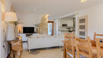Un salon moderne avec un canapé, une table à manger et des chaises, une cuisine en arrière-plan et un mur d’accent en pierre.