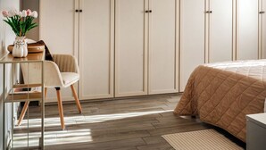 Ein Schlafzimmer mit Bett, Kleiderschrank, Schreibtisch mit Stuhl und Pendelleuchte.