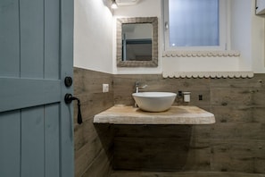 A bathroom with a wooden vanity, a white sink, a mirror, and a door. - GuestHost - Cozy 35 sqm apartment, perfect for four people, located on the ground floor of a building (access via one step).The property is located in Visgnola, a quiet village near Bellagio, one of Lake Como's most popular destinations. It's well-served (Bellagio)
