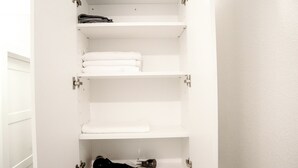 Een witte kast met meerdere planken, waarvan sommige gevuld zijn met opgevouwen handdoeken en een zwart voorwerp op de onderste plank.