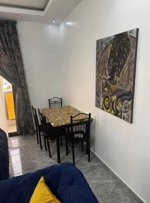 A dining area with a table and chairs, a painting on the wall, and a blue sofa with a yellow pillow. - Charming 2-bedroom apartment in the heart of Dakar (Dakar)