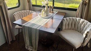 Un espace repas comprenant une table, des chaises et une vue sur un champ verdoyant, visible à travers de grandes fenêtres.