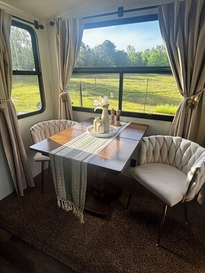 A dining area with a table, chairs, and a view of a green field through large windows.