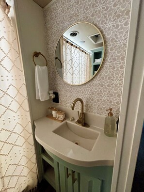 A bathroom with a round mirror, a sink, a towel ring, and a toilet. - Cozy Getaway on a quiet pasture minutes from Callaway Gardens. (Pine Mountain Valley)