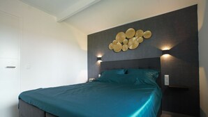 Une chambre moderne avec un grand lit, une tête de lit sombre et des luminaires fixés au mur.