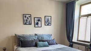 Une chambre à coucher avec un lit, un tapis rond et trois œuvres d’art florales encadrées accrochées au mur.