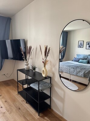Une chambre à coucher comprenant un lit, une télévision, un miroir et une console sur laquelle sont disposés des objets décoratifs.