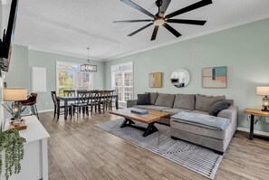 A spacious living room with a modern sofa, a dining area with a wooden table, and a ceiling fan. - NEW! 2 min walk to Beach + 2 King Master Suites + Family Friendly (Surfside Beach)