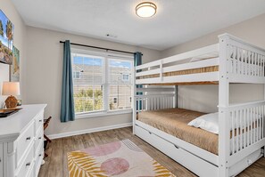 A room with a bunk bed, a desk with drawers, a lamp, a window with curtains, and a view of greenery outside. - NEW! 2 min walk to Beach + 2 King Master Suites + Family Friendly (Surfside Beach)
