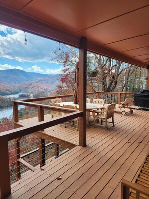 Eine Holzterrasse mit Tisch und Stühlen mit Blick auf einen See und Berge.