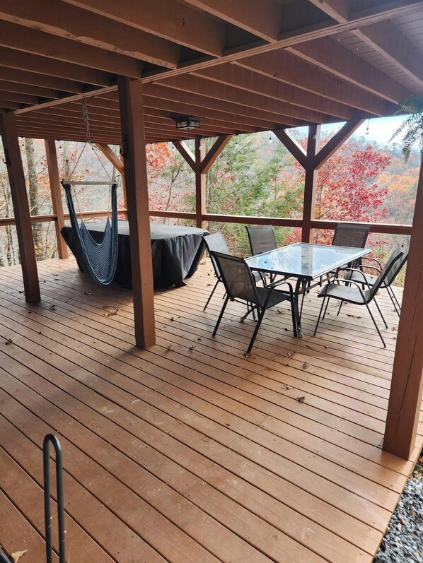 Eine Holzterrasse mit Tisch und Stühlen, einer Hängematte und Blick auf Herbstlaub.