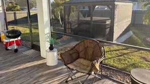Un'area patio coperta con una griglia, una sedia imbottita e un piccolo giardino.