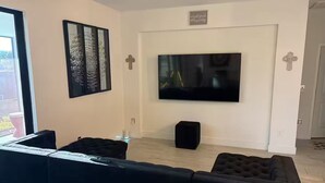 Un soggiorno moderno con una grande TV a schermo piatto montata a parete, un divano modulare nero e un piccolo poggiapiedi nero.