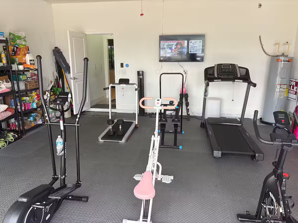 A home gym with various exercise equipment including a treadmill, elliptical, and stationary bike.