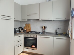 A modern kitchen with white cabinets, a gas stove, an oven, and a sink. - Spring Apartment (Rapallo)