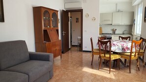 Un salon avec un canapé gris, un meuble en bois et un coin repas comprenant une table et des chaises.