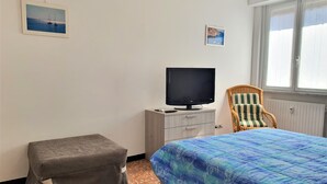 Une chambre à coucher avec un lit, un téléviseur posé sur une commode, une chaise et deux tableaux encadrés accrochés au mur.