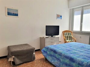A bedroom with a bed, a TV on a dresser, a chair, and two framed pictures on the wall. - Spring Apartment (Rapallo)