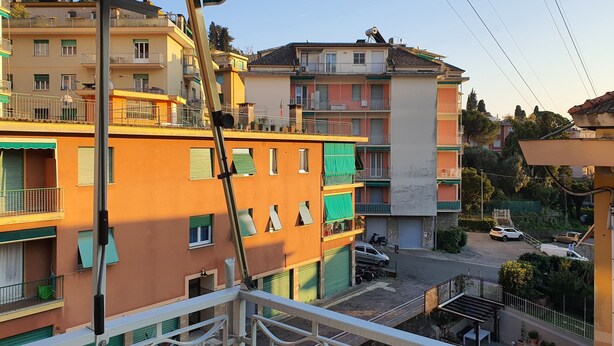 Un immeuble résidentiel à plusieurs étages, doté de balcons, d’un auvent vert et donnant sur la rue, où l’on peut voir des voitures garées et de la verdure.