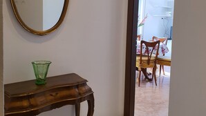 Un couloir avec une console en bois, un vase en verre vert et un miroir à cadre doré.