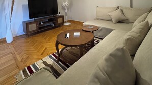 Un salon moderne comprenant un canapé, deux tables basses, un téléviseur et un ventilateur.