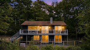 A two-story house with a balcony, large windows, and a wooden deck. - Lake Views & Mountain Adventures Await (Gilford)