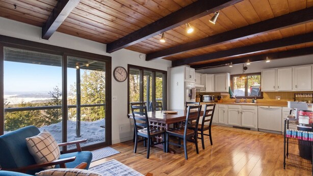 A spacious living area with a large dining table, blue chairs, and a view through large windows. - Lake Views & Mountain Adventures Await (Gilford)