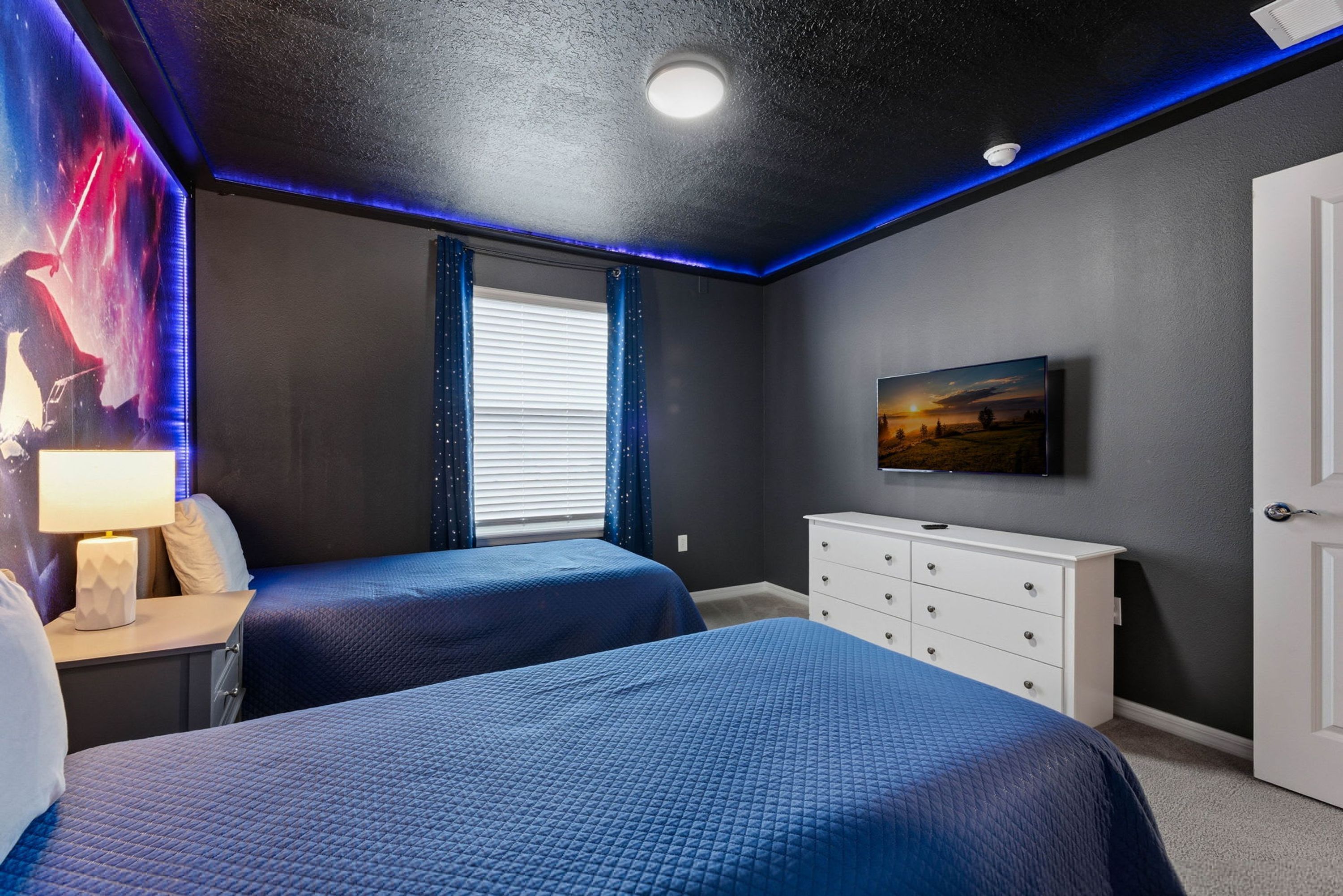 A bedroom with two beds, a dresser, a TV, and a window with curtains.