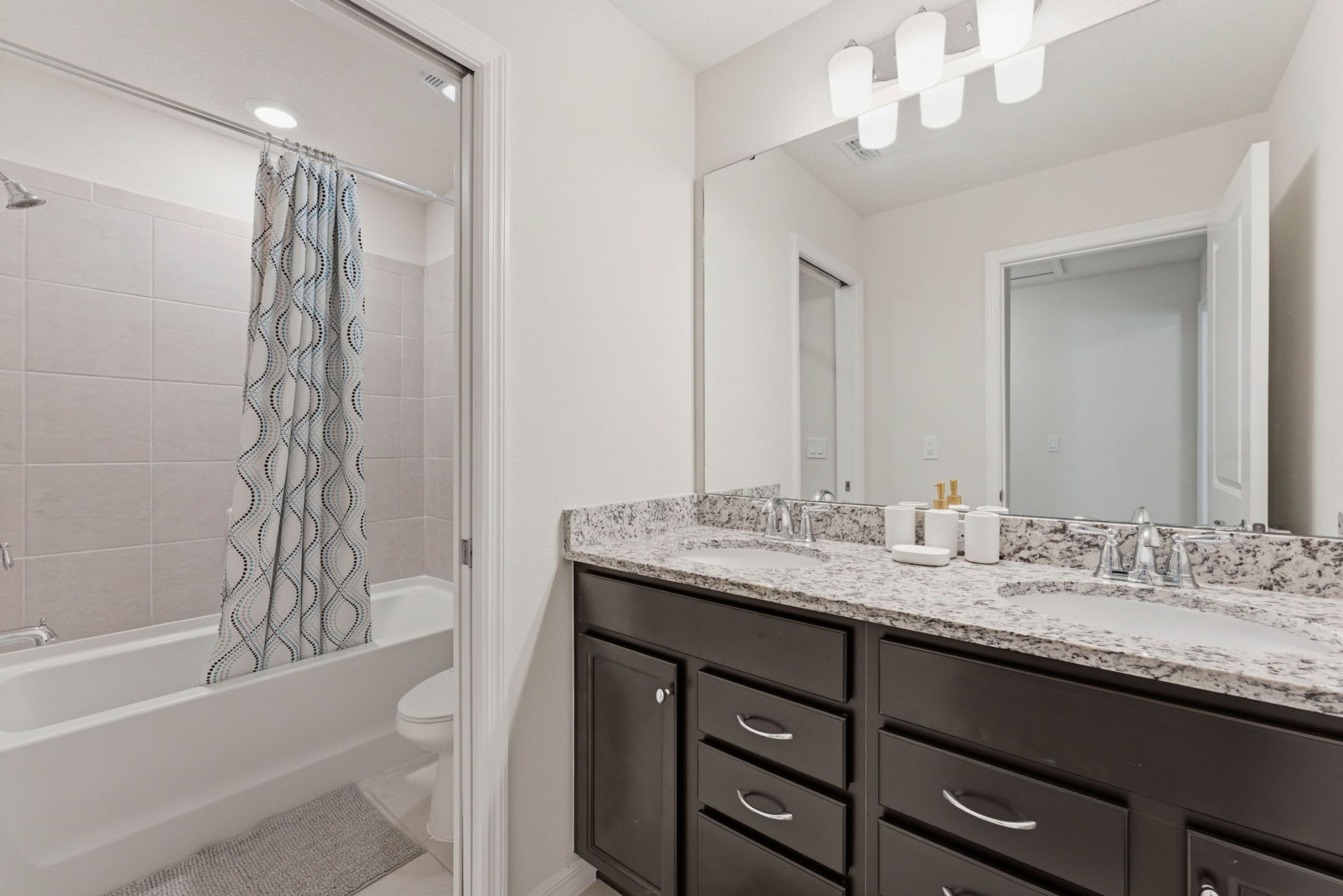 Un baño moderno con bañera, ducha, inodoro, muebles oscuros y un espejo grande.