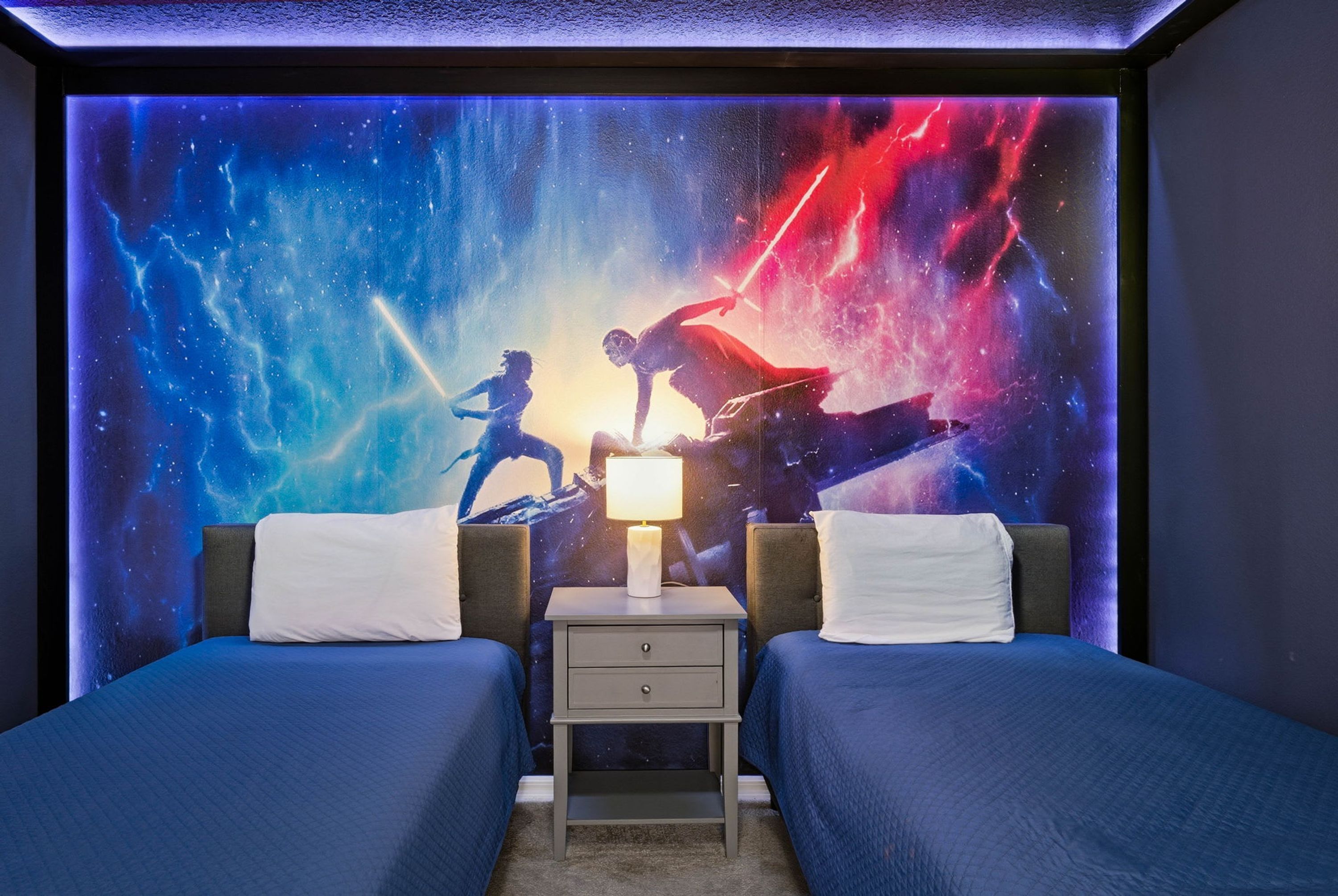A bedroom with two beds, a nightstand, and a wall mural of a space scene.