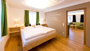 A modern bedroom with a wooden bed, green curtains, a wall with a motivational quote, and a view into a living area with a green sofa. - Heavenly vacation - living in the vicarage (Sölk)
