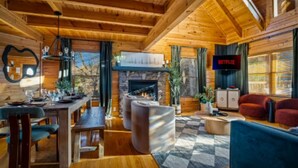 Ein gemütliches Blockhaus-Interieur mit einem Essbereich aus Holz, einem Kamin, einem Wohnzimmer mit einer Couch und einem an der Wand befestigten Fernseher.
