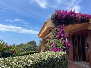 A building with a wooden balcony, a stone wall, and a hedge. - Villa Daiva Sunset Paradise & Pool (Costa Paradiso)
