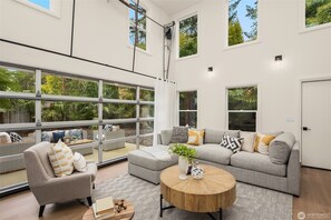 Amplia sala de estar con ventanas grandes, un sofá gris, un sillón y una mesa de centro.
