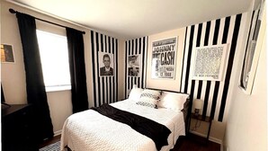 Ein Schlafzimmer mit einem Bett, Wänden im Streifenmuster aus Schwarz und Weiß sowie Postern.