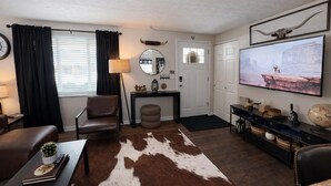 Ein modernes Wohnzimmer mit einer Ledersofa, einem runden Couchtisch, einem Kuhfellteppich, einem Fernseher und einem Konsolentisch mit Dekorationen.