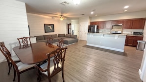 Una cocina moderna con armarios de madera, una isla central y un comedor con mesa y sillas de madera.