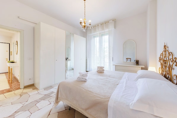 A hotel room with a bed, a bedside table, a mirror, and a chandelier. - Guesthost - Il Salotto Blu - Appartamento Con Parcheggio (Florence)