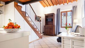 Una cocina con una escalera de madera, una encimera blanca con un frutero, un armario de madera y un comedor con mesa y sillas.