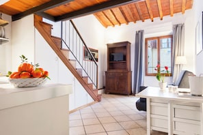 A kitchen with a wooden staircase, a white countertop with a fruit bowl, a wooden cabinet, and a dining area with a table and chairs. - Guesthost - Appartamento Pazzi A 3 Min Da Piazza Del Duomo (Florence)