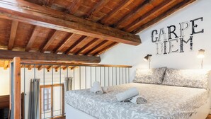Un dormitorio con cama, vigas de madera, un letrero en la pared y una ventana con cortinas.