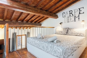 A bedroom with a bed, wooden beams, a wall-mounted sign, and a window with curtains. - Guesthost - Appartamento Pazzi A 3 Min Da Piazza Del Duomo (Florence)