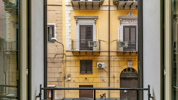Ein gelbes Gebäude mit Balkonen, einer braunen Tür und einem Fenster mit Rollläden.