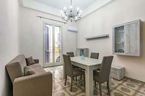 A dining area with a table, chairs, a chandelier, a sofa, and a cabinet. - Guesthost - Teatro Massimo Roomy Flat With Covered Terrace (Palermo)