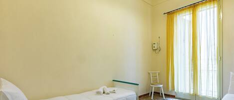 Une chambre avec un lit simple, une chaise, une table de chevet et une fenêtre avec des rideaux jaunes.