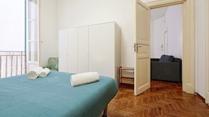 A bedroom with a bed, a wardrobe, a small table, and a sofa in the adjacent room. - Guesthost - Teatro Massimo Lovely Flat With Balconies (Palermo)